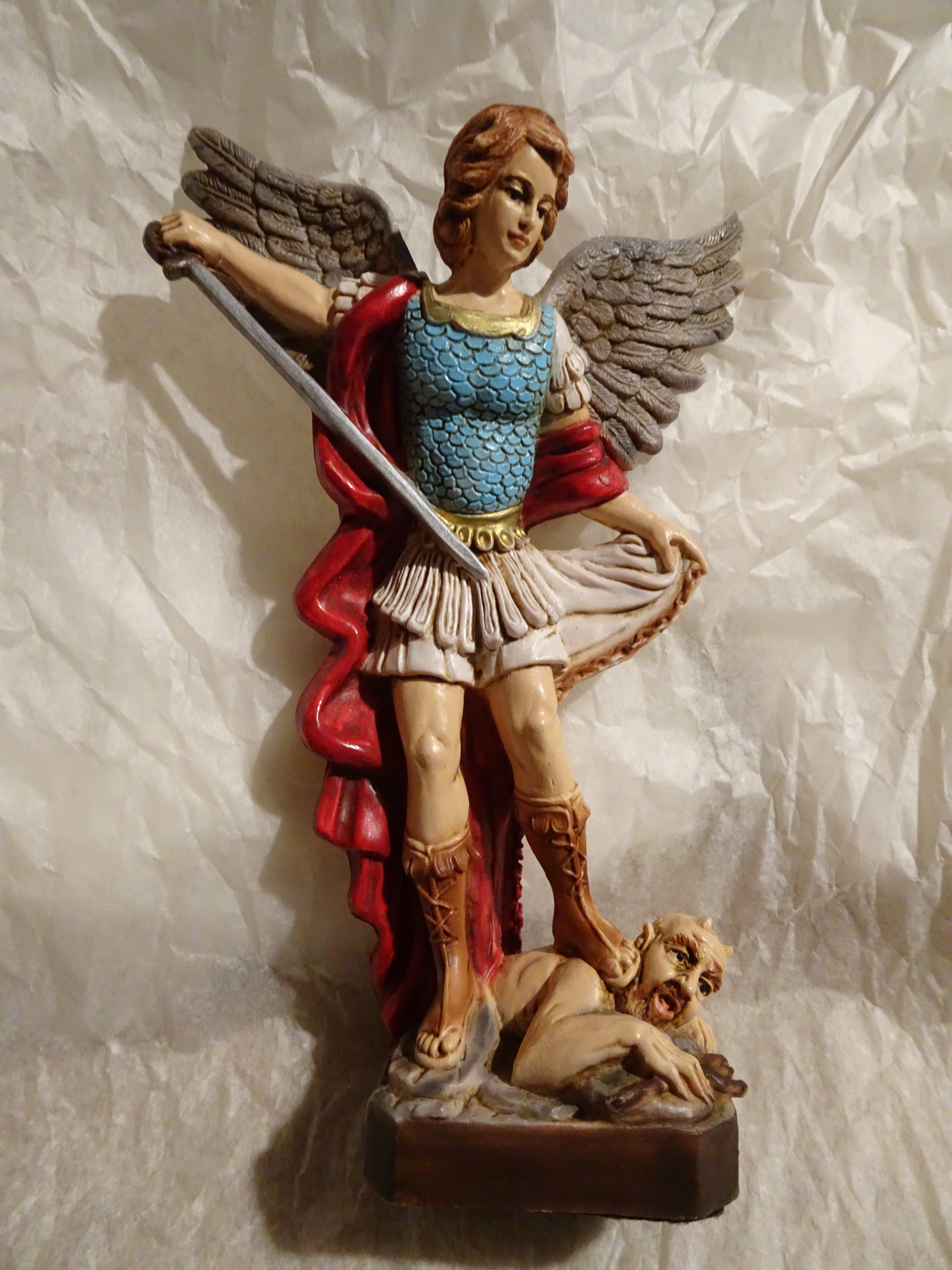 Polychrome resin figure of a female St Michael standing over Satan, with drawn sword, holding her skirt/mantle out with her left hand.